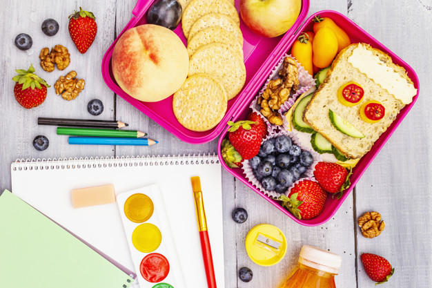 School lunch box with sandwich, fresh fruits, vegetables, cookies, juice and nuts. Healthy eating habits for kids. Back to school concept. With school supplies, wooden boards background, top view